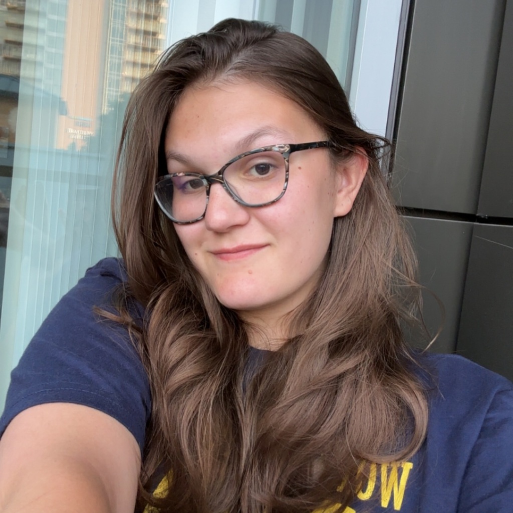 A picture of Elisa, taken as a selfie. She is in front of a window. She is wearing a dark t-shirt with yellow lettering.