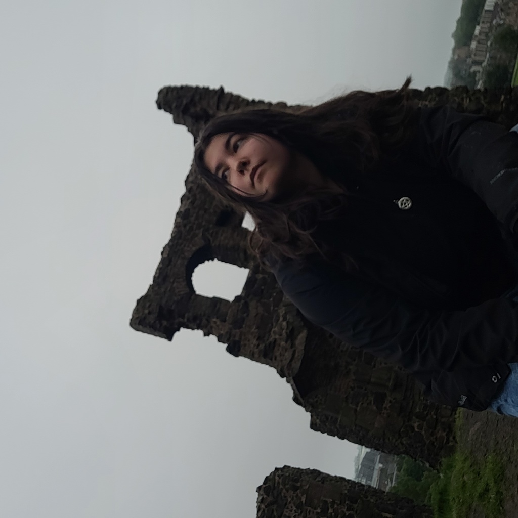 A picture of Alyssa standing in front of the remains of an old stone building. She is looking off into the distance.