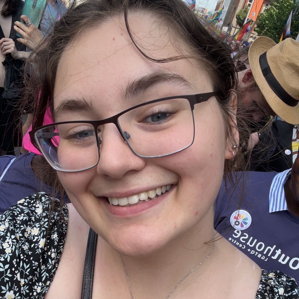 A picture of Katy with her hair pulled back. She is at an event and surrounded by a crowd. She is smiling.