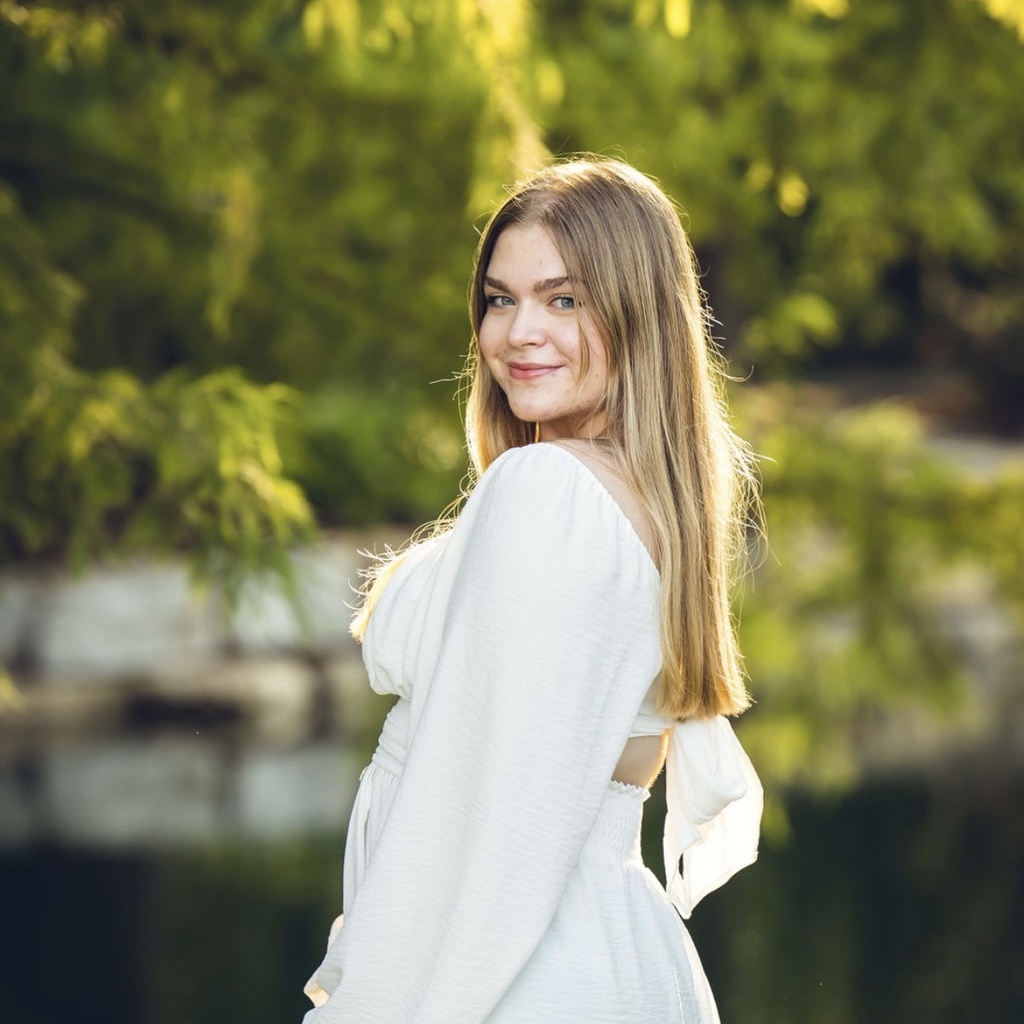A picture of Kylie standing in side profile, head turned toward the camera. She is wearing a loose white dress with her hair down and smiling.